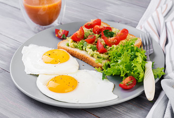 Breakfast. Fried egg, vegetable salad and a grilled avocado sandwich on a grey background.