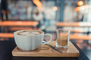 Hot Coffee cup and brown sugar on the wooden tray in coffee shop background