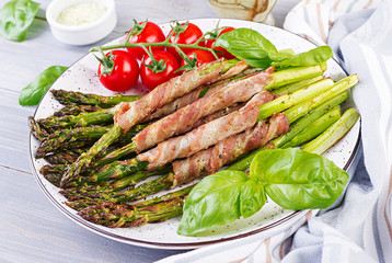 Grilled green asparagus wrapped with bacon on wooden table.
