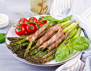 Grilled green asparagus wrapped with bacon on wooden table.