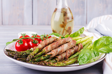 Grilled green asparagus wrapped with bacon on wooden table.