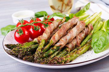 Grilled green asparagus wrapped with bacon on wooden table.