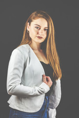 Junge Frau selbstbewusst, mit Jeans und weißem Blazer lächelt in die Kamera.