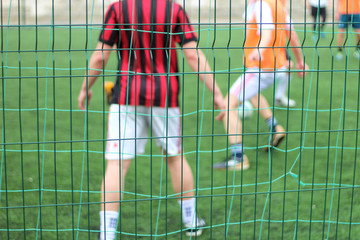 Focused image of sectional green fence. Soccer players with a ball plays on the background.