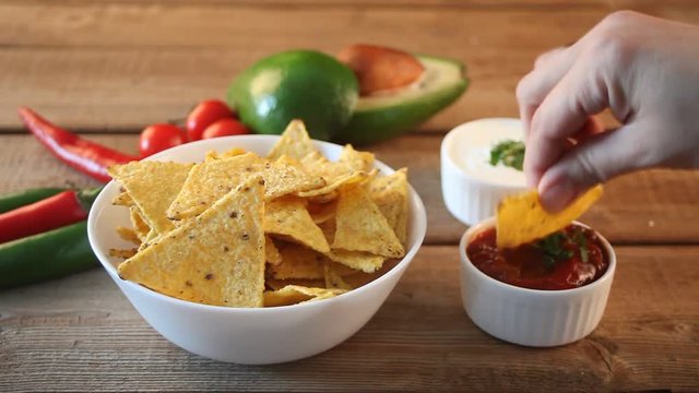 Woman hand takes Mexican chips nachos and dips in a sause salsa