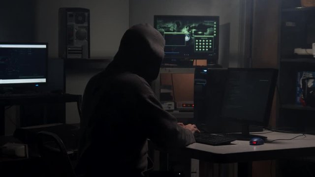 Computer Hacker types in computer code in a back room