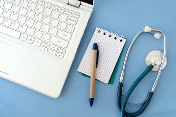Laptop white, stethoscope, paper and pen on blue background. The concept of transition to modern...