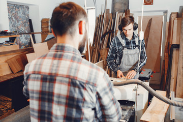 Two men carves a tree. The carpenters works in a studio. An engineer provides a tree shape