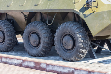 Close-up on rubber tires with a large tread to overcome impassable roads and dirt on a Russian-made green armored personnel carrier on a clear summer day. War and military equipment.