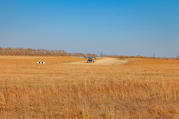 Obraz premium A small aircraft for the transport of passengers and paratroopers lands in a field on a landing strip with grass under a blue sky above the trees on a clear cloudless day. Air patrol.
