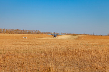 A small aircraft for the transport of passengers and paratroopers lands in a field on a landing strip with grass under a blue sky above the trees on a clear cloudless day. Air patrol.