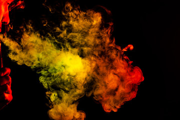 Portrait of a side mouth part of guys face with a colored backlight of monochrome smoking a vape and exhaling white red and yellow in different directions on a black isolated background.