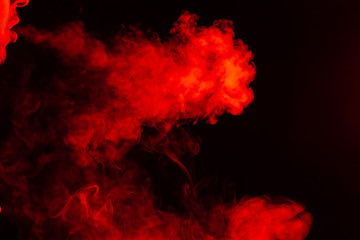 Portrait of a side mouth part of guys face with a colored backlight of monochrome smoking a vape and exhaling white red in different directions on a black isolated background. Puffs harmful to health.