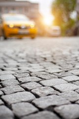 An unfocused yellow cab at the background of the street with cobblestones on a sunny afternoon