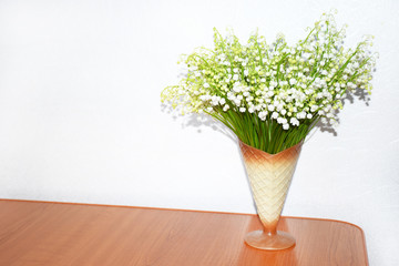 White lilies of the valley in a vase in the shape of a horn for ice cream on a white background. Spring Flowers Background with space for text.