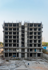 construction site of a modern tall residential building with workers working in the apartment block with the steel rods scattered on the ground.
