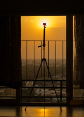 Silhouette of a action camera mounted on a tripod for taking a time lapse of a sunset or sunrise from a tall residential apartments balcony.