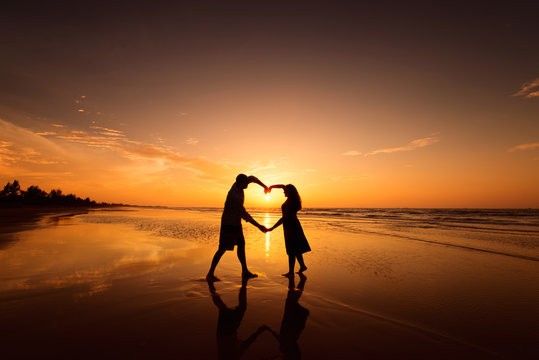 Silhouette of couple making heart shape with arms on beach at sunset