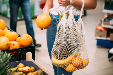 Woman with mesh bag full of fresh vegetables shopping at the store, zero waste concept