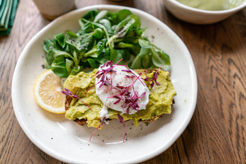Morning in cafe, oak table. Healthy breakfast with wholemeal bread toast with avocado, poached egg with green salad. Green tea on the Background.