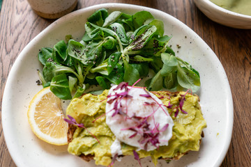 Morning in cafe, oak table. Healthy breakfast with wholemeal bread toast with avocado, poached egg with green salad. Green tea on the Background.