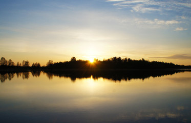 Fototapeta na wymiar Beautiful sunset on the forest lake. The sun is reflected in the water. Bright contrasting sky.