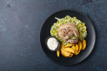 Boiled knuckle, served with cabbage and baked potatoes. Top view. Darkblue background. Dark mod.