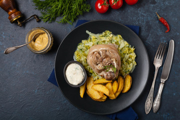 Boiled knuckle, served with cabbage and baked potatoes. Top view. Darkblue background. Dark mod.