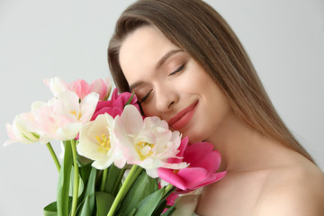 Young woman with bouquet of beautiful tulips on light background