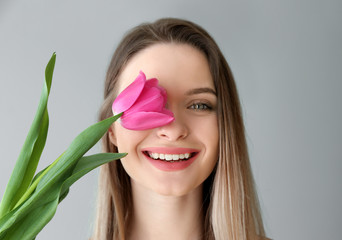 Young woman with beautiful tulip on light background