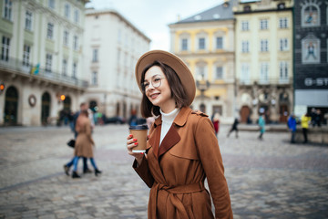 Fototapeta premium Cheerful young woman in the street drinking morning coffee in sunshine light