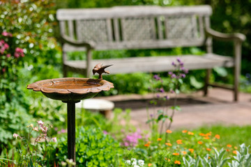 Idyllic view of a beautiful green and growing  springtime garden with flowering plants, grass and a bird bath and a wooden bench on a sunny day