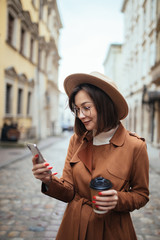 Portrait of a pretty smiling woman using mobile phone while holding coffee cup on a city street