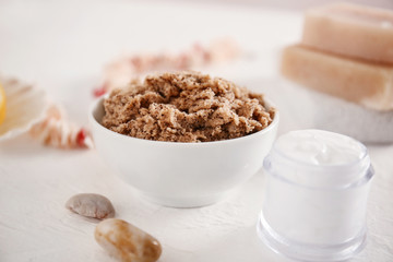 Bowl with body scrub and cream on table