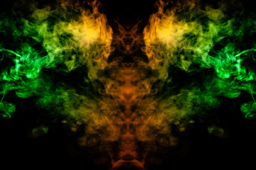 Smoke of different green, yellow, orange and red colors in the form of horror in the shape of the head, face and eye with wings on a black isolated background. Soul and ghost in mystical symbol