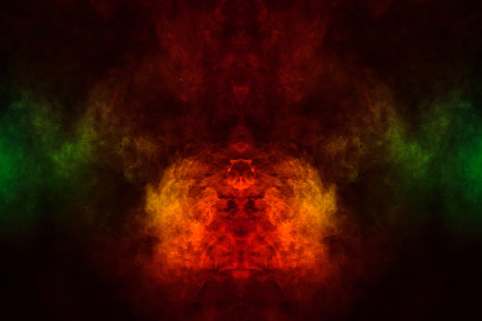 Abstract image of smoke of different green, yellow, orange and red colors in the form of horror in the shape of the head, face and eye on a black isolated background. Soul and ghost in mystical symbol