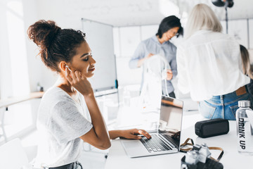 Obraz premium Pleased african female manager relaxing with eyes closed in headphones during coffee break. Indoor portrait of young office workers of international company resting after hard day.
