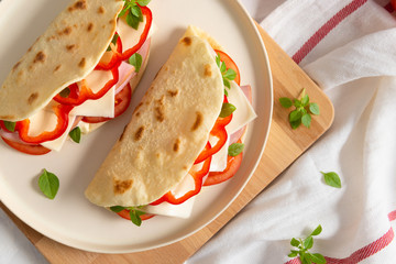 homemade italian piadina on a white plate with vegetables tomatoes and pepper on white background. Italian cuisine. Top view, copy space. flat lay