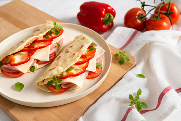 Piadina romagnola - Italian flatbread with prosciutto, tomato, basil, pepper and cheese on white background. Copy space