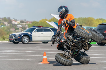 Extreme acrobatics on a Quad bike. A teenage child performs tricks on a Quad bike. The Quad bike is on two wheels sideways. On the back the background of a police car