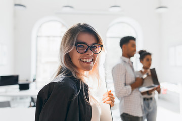 Close-up portrait of smiling female student in trendy glasses holding documents on blur background. Black young man working as manager carrying laptop to office.