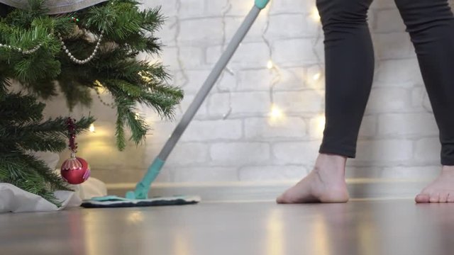 girl is preparing for holiday, she washes floor on background of Christmas fir. Close-up