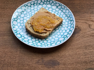 Bread toast with peanut butter and orange jam on a blue plate. Wooden table copy space 