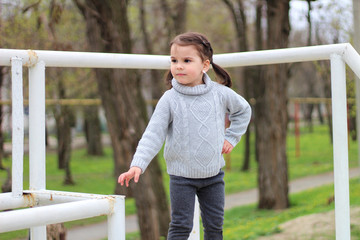 Obraz premium little cheerful brunette girl in a sweater and with tails is standing on a metal structure on construction site