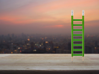 Green pencil ladder on wooden table over blur of cityscape on warm light sundown, Business success concept