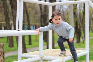 Obraz premium little cheerful brunette girl in a sweater and with tails is climbs on a metal structure on construction site