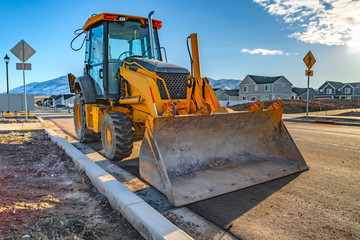 Yellow loader with homes and mountain against blue sky in the background