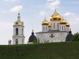 Fototapeta na wymiar Dmitrov Kremlin. Tourists man and woman studying the map against a clear sky, a beautiful white Orthodox Church with Golden domes and a bell tower in summer on a clear Sunny day