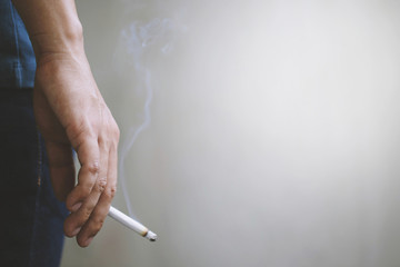 man holding smoking a cigarette in hand. Cigarette smoke spread. dark background