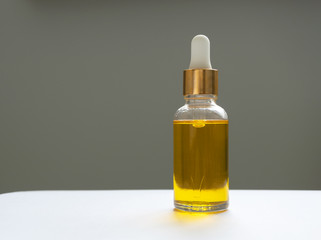 Oil serum in glass bottle with pipette. Yellow essence on gray background